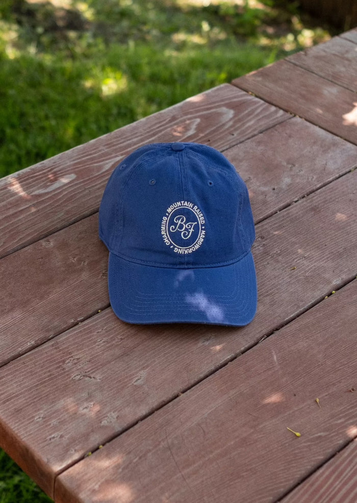 Blue Mountain Raised baseball cap with a white circular logo on the front resting on a wooden surface.